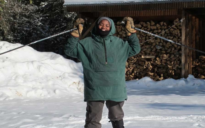 a person wearing snow gear stands on snowy ground and raises ski poles in the air